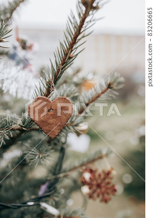 Handmade gingerbread heart shaped cookie decoration on a Christmas tree. Outdoor background without snow. Diy creative ideas for children. Environmental concept. Selective focus, copy space Handmade gingerbread heart shaped cookie decoration on a Christmas tree. Outdoor background without snow. Diy creative ideas for children. Environmental concept. Selective focus, copy space 83206665