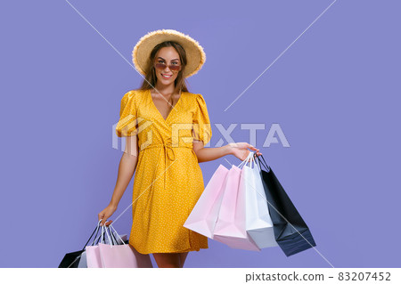 Happy woman in hat and sunglasses holds purchases while smiling at camera. Black Friday, big sales Happy woman in hat and sunglasses holds purchases while smiling at camera. Black Friday, big sales 83207452