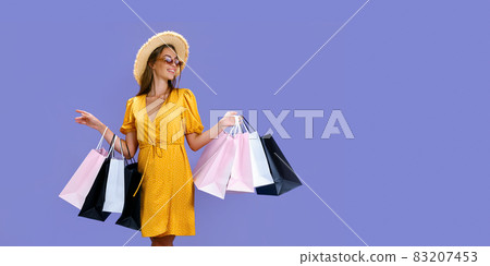 Pretty woman in sunglasses and hat holds colourful shopping bags on purple background. Sales concept 83207453