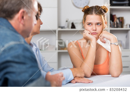Adult couple is carefully talking with a sad daughter at the table Adult couple is carefully talking with a sad daughter at the table 83208432