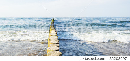 A bird sits in the distance on a wooden breakwater in a rough sea, seascape with a sea horizon 83208997