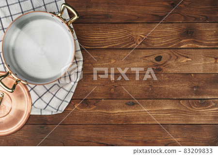 New copper cooking pot on wooden table, view from above New copper cooking pot on wooden table, view from above 83209833
