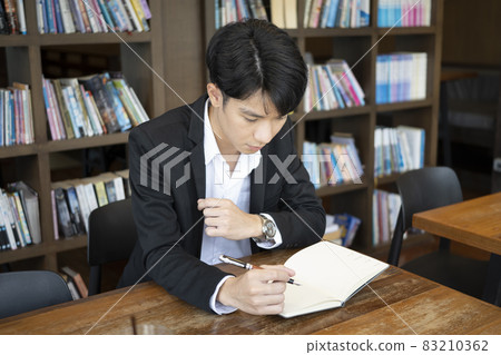 Young businessman in suit holding pen and writing information on notebook. Young businessman in suit holding pen and writing information on notebook. 83210362