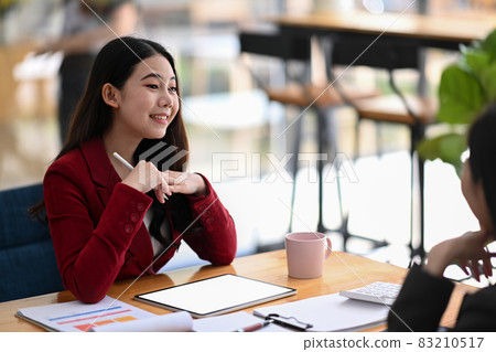 Cheerful businesswoman working with her colleague in modern office. Cheerful businesswoman working with her colleague in modern office. 83210517