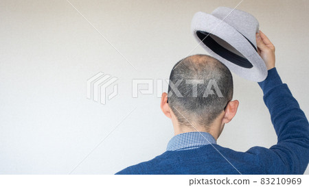 A Japanese man with thin hair and a shaved head takes off his hat and says hello 83210969