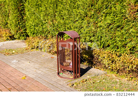 Metal rubbish bin by bushes in park Metal rubbish bin by bushes in park 83212444