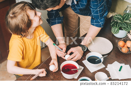 Easter day. Father and son painting eggs on wooden background. Family sitting in a kitchen. Preparing for Easter, creative homemade decoration Easter day. Father and son painting eggs on wooden background. Family sitting in a kitchen. Preparing for Easter, creative homemade decoration 83214172