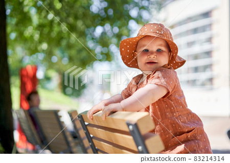 Portraits of a cute 10 months old baby girl. Walking on the playground, on a sunny summer day. 83214314