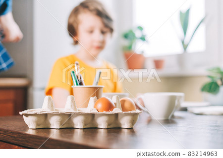 Easter day. Kid boy painting eggs on wooden background. Child sitting in a kitchen. Preparing for Easter, creative homemade decoration Easter day. Kid boy painting eggs on wooden background. Child sitting in a kitchen. Preparing for Easter, creative homemade decoration 83214963