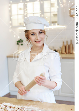 a cheerful chef prepares a Christmas cake. Lady cook in a cute apron breaking an egg into flour to make cake. The process of cooking. Step by step. Unsurpassed pre-holiday atmosphere and home comfort a cheerful chef prepares a Christmas cake. Lady cook in a cute apron breaking an egg into flour to make cake. The process of cooking. Step by step. Unsurpassed pre-holiday atmosphere and home comfort 83215430