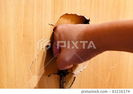 A man's hand punched a hole in the plywood wall. The concept of aggression and overcoming problems. 83216174