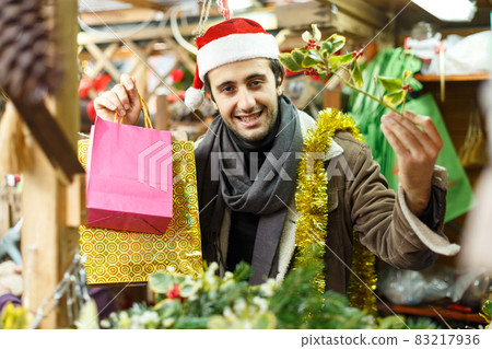 Happy young man Christmas hat with looking toys at fair outdoor Happy young man Christmas hat with looking toys at fair outdoor 83217936