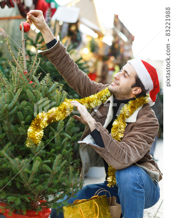 Portrait of joyful man choosing toys and Christmas tree at fair 83221988