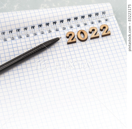 Notebook and pen on the table. Wooden numbers date 2022. A blank sheet of paper and a ballpoint pen. 83223175