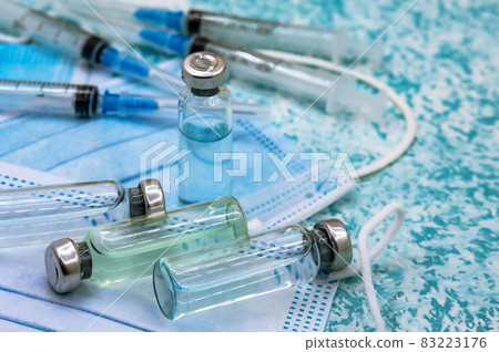 Medical vials, syringes and mask on a green background. Prevention of seasonal diseases. Vaccination against covid-19. 83223176