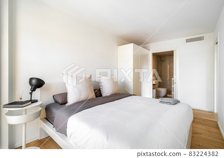 Bright bedroom with cozy bed, big pillows, wardrobe and bathroom. Interior of modern apartment in European city. 83224382