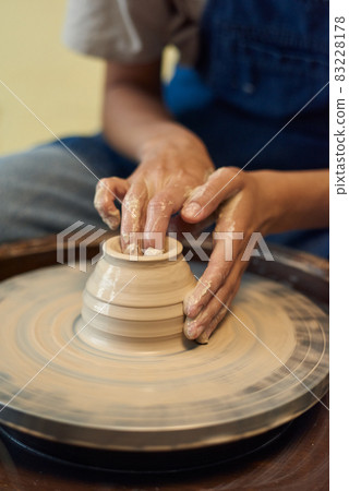 Close-up of unrecognizable potter with wet dirty hand molding walls of clay pot on pottery wheel 83228178