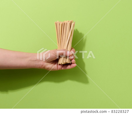 female hand holds disposable wooden sticks for stirring hot drinks on a green background. Coffee and tea spoon female hand holds disposable wooden sticks for stirring hot drinks on a green background. Coffee and tea spoon 83228327