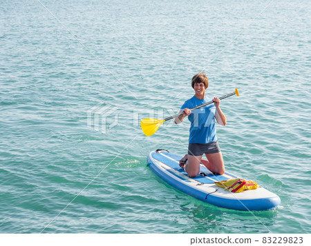 Paddle boarder. Sportsman on knees paddling on stand up paddleboard. SUP surfing. Active lifestyle. Outdoor recreation. Vacation on seaside. Paddle boarder. Sportsman on knees paddling on stand up paddleboard. SUP surfing. Active lifestyle. Outdoor recreation. Vacation on seaside. 83229823