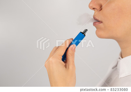 Caucasian woman smokes disposable vape on white background. Alternative device for smoking. 83233080