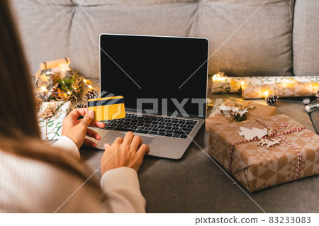 Close up of woman hands with credit card, gifts, and mock up screen laptop. Online shopping at Christmas holidays. Cropped female sit on couch with natural eco presents and decor. Merry Christmas Close up of woman hands with credit card, gifts, and mock up screen laptop. Online shopping at Christmas holidays. Cropped female sit on couch with natural eco presents and decor. Merry Christmas 83233083