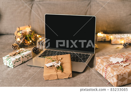 Online shopping at Christmas holidays. Gifts, and mock up screen laptop on couch with natural eco presents and decor. Merry Christmas. Wrapping present boxes. Online shopping at Christmas holidays. Gifts, and mock up screen laptop on couch with natural eco presents and decor. Merry Christmas. Wrapping present boxes. 83233085