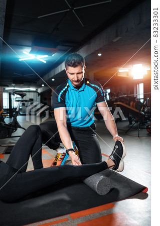 young female relaxing with myofascial release roller with trainer in gym 83233301