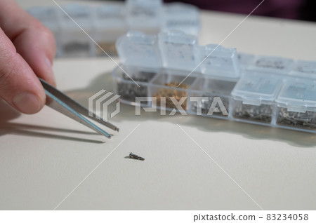 A close-up of male hands takes a screw for repairing glasses with tweezers A close-up of male hands takes a screw for repairing glasses with tweezers 83234058