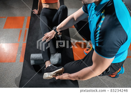 young female relaxing with myofascial release roller with trainer in gym 83234246