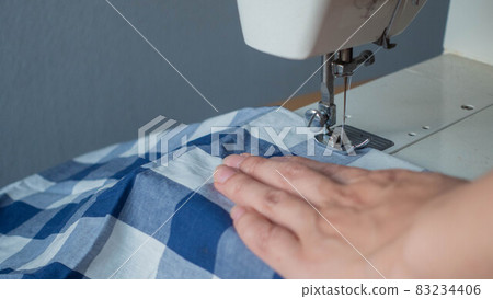 Female hand operating an electric sewing machine Female hand operating an electric sewing machine 83234406