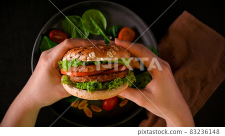 Close-up hands holding tasty vegan burger, soy protein burger with fresh vegetables 83236148