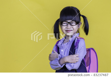 Portrait of young happy little cute asian girl in school uniform isolated on yellow background with copy space. Education for toddler or preschool, childhood lifestyle back to school concept Portrait of young happy little cute asian girl in school uniform isolated on yellow background with copy space. Education for toddler or preschool, childhood lifestyle back to school concept 83237487