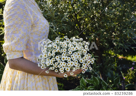 A young woman in a light dress holds a bouquet of wildflowers. Beauty in nature. Side view. Copy space 83239286