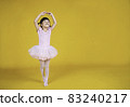 Portrait of little asian child girl dreams of becoming ballerina in a pink tutu skirt isolated on yellow background. Happy young girl practise her dance. Education childhood toddler lifestyle concept 83240217