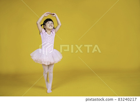 Portrait of little asian child girl dreams of becoming ballerina in a pink tutu skirt isolated on yellow background. Happy young girl practise her dance. Education childhood toddler lifestyle concept 83240217