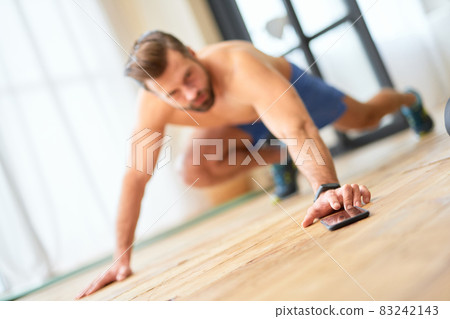 Athletic young man using mobile phone during workout at home 83242143