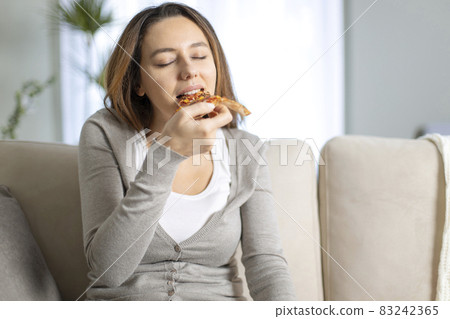 Beautiful young girl eating a slice of pizza at home 83242365