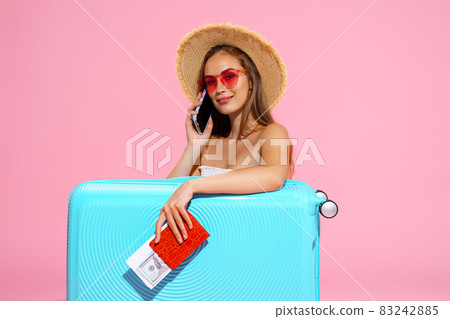 Glad girl with suitcase, tickets, money and passport are going to travel while speaking on phone Glad girl with suitcase, tickets, money and passport are going to travel while speaking on phone 83242885