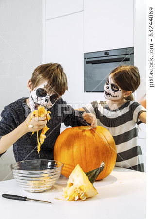 Kids with skull face paint carving a pumpkin Kids with skull face paint carving a pumpkin 83244069