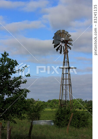 Kansas Windmill with blue sky and white clouds with tree's north of Hutchinson Kansas USA. 83245135