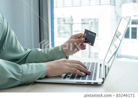 The businesswoman's hand is holding a credit card and using a laptop for online shopping and internet payment in the office 83246171