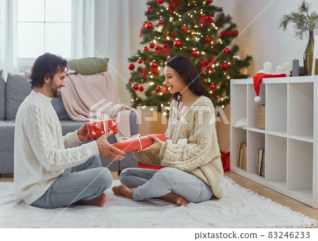 Couple Celebration New Year Near Christmas Tree at Home, Exchange Presents in the Gift Boxes 83246233