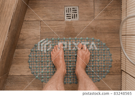 Men's feet stand on a plastic anti-slip mat next to the floor drain in the bathroom or shower Men's feet stand on a plastic anti-slip mat next to the floor drain in the bathroom or shower 83248565