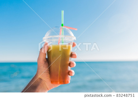 The guy's hand holds a colored chilled non-alcoholic cocktail against the background of the sea 83248751