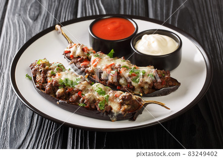 Portion of eggplant stuffed with meat, vegetables and baked with cheese served with sauces close-up in a plate. horizontal 83249402