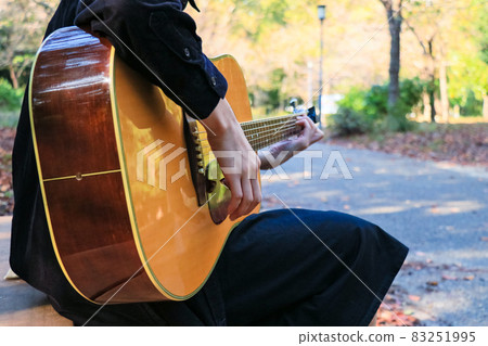 A woman playing an acoustic guitar in the woods 83251995