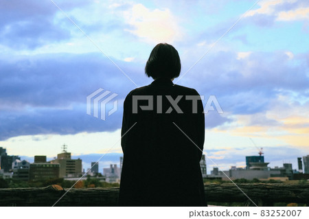 一個女人看著傍晚的天空和城市景觀的剪影 83252007