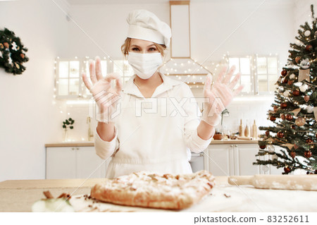 a cheerful chef prepares a Christmas cake. Lady cook in a cute apron breaking an egg into flour to make cake. The process of cooking. Step by step. Unsurpassed pre-holiday atmosphere and home comfort 83252611