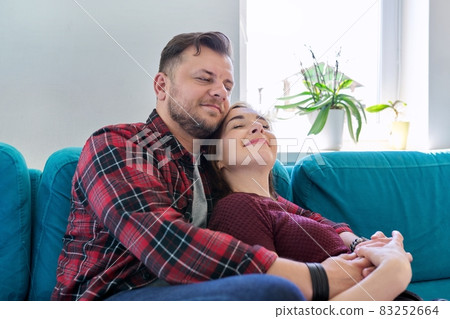 Happy middle-aged couple embracing at home on the couch Happy middle-aged couple embracing at home on the couch 83252664