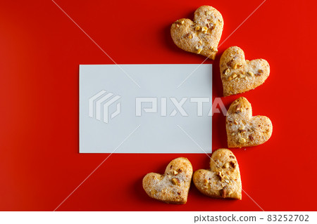 Cookies on a red background and a blank greeting card. Empty greeting card and heart-shaped cookies on a red background. Place for text 83252702